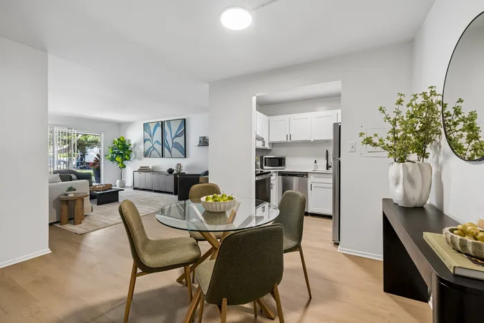 Modern open-plan living room and kitchen with elegant decor, featuring a glass dining table and lush greenery, ideal for stylish apartment living.