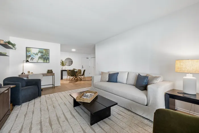 Inviting living room area with a cozy beige sofa, chic decor, and modern dining space in the background, complemented by a stylish abstract painting.