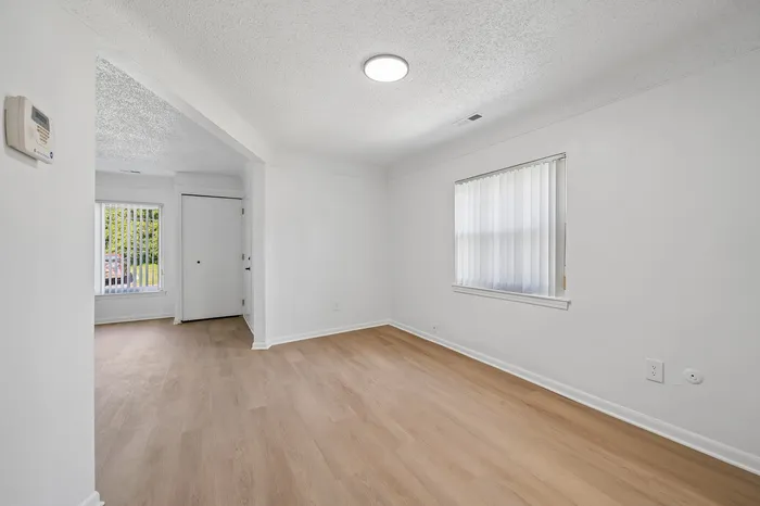 Bright and welcoming empty room with fresh white walls and stylish wood flooring, featuring two large windows allowing ample natural light.