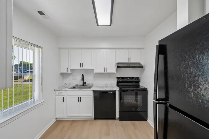 Bright kitchen featuring modern black appliances, sleek white cabinetry, and elegant marble countertops with a view of the lush green outdoors.