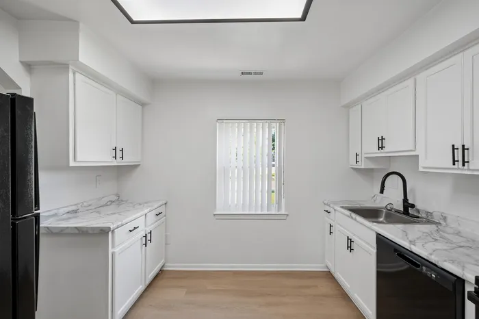 Bright and modern kitchen with sleek white cabinetry, marble countertops, and ample natural light from the window.