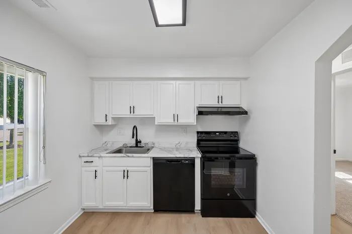Bright and modern kitchen with sleek black appliances, elegant white cabinetry, and a large window for natural light.