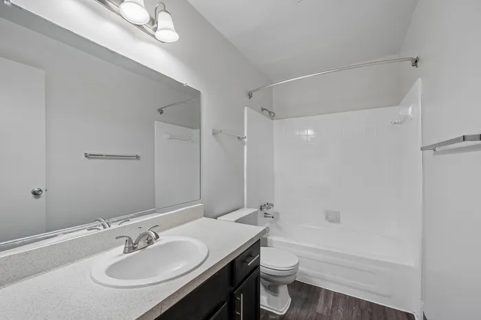Modern bathroom with elegant white fixtures, large mirror, and chic lighting, featuring a pristine bathtub and sleek vanity.