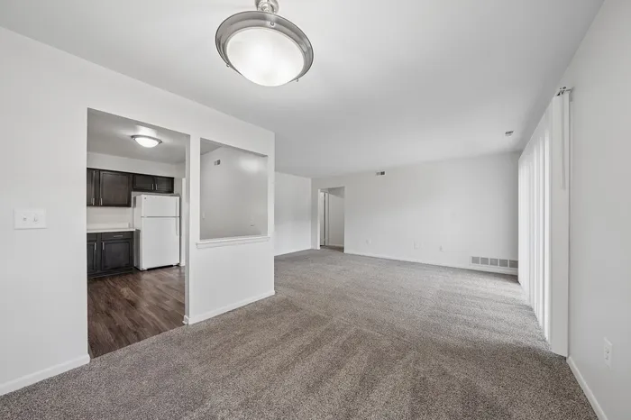 Bright and spacious living area with plush carpeting and an inviting kitchen featuring modern dark cabinets and sleek appliances.