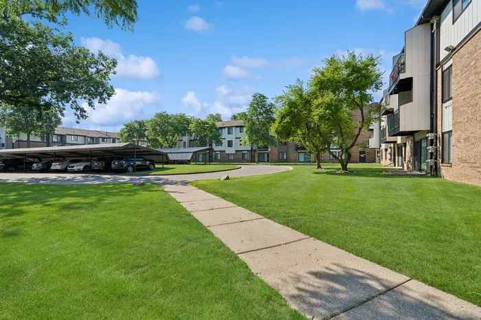 Sunny apartment complex with well-maintained green lawns, covered parking, and inviting sidewalks in a serene neighborhood.
