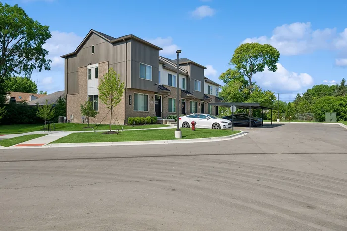Beautiful modern townhouse complex with sleek architecture, lush green lawn, and spacious parking area under a clear blue sky.