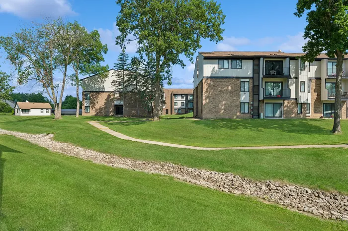 Charming apartment complex surrounded by lush green lawns, mature trees, and vibrant blue skies, offering a serene and inviting atmosphere.