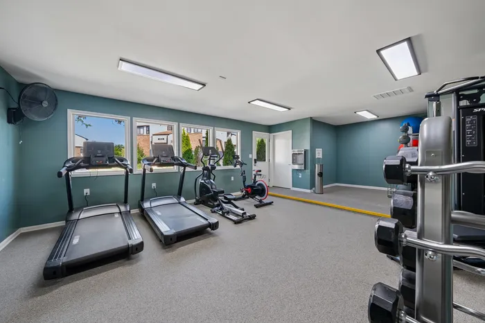 Modern fitness room featuring state-of-the-art exercise machines, including treadmills, elliptical, and a stationary bike, with a bright and inviting atmosphere.