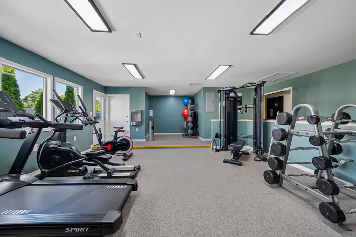 Bright and modern gym area with state-of-the-art exercise equipment, including treadmills, bikes, and a weight rack, ideal for fitness enthusiasts.