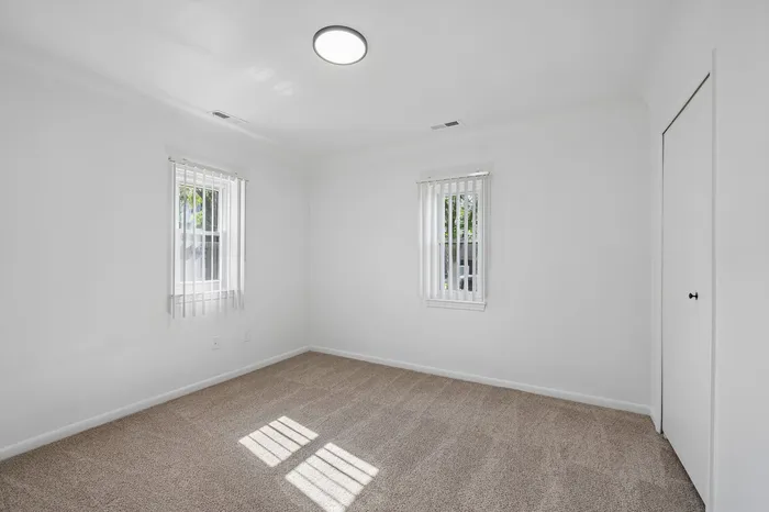 Bright, pristine bedroom with plush carpet, ample natural light, and modern blinds creating a tranquil retreat.