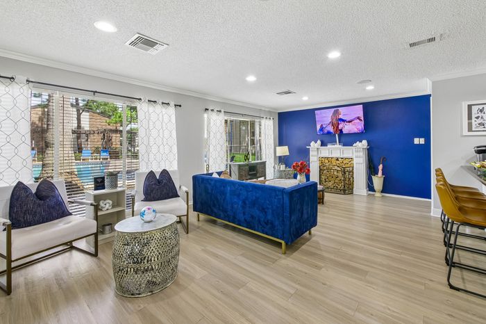 Bright and inviting living room with a modern flair featuring a plush blue sofa, elegant fireplace, and large windows offering a scenic view of the pool area.