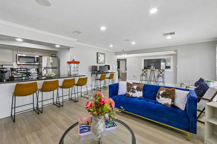 Chic open-concept living area with modern kitchen, stylish bar stools, and a plush blue sofa, ideal for entertaining.