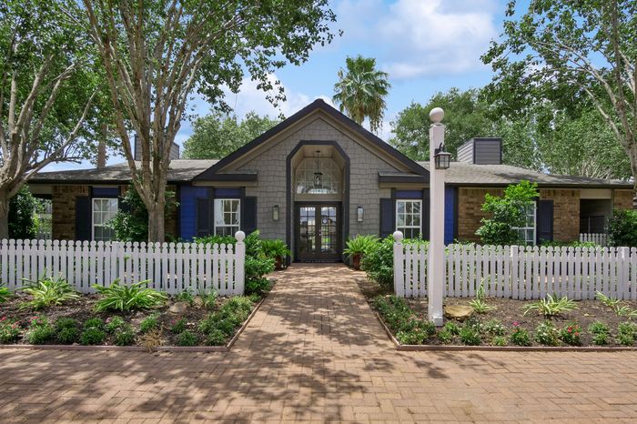 Charming suburban home with picturesque landscaping and a welcoming pathway leading to the entrance, framed by a white picket fence and lush greenery.