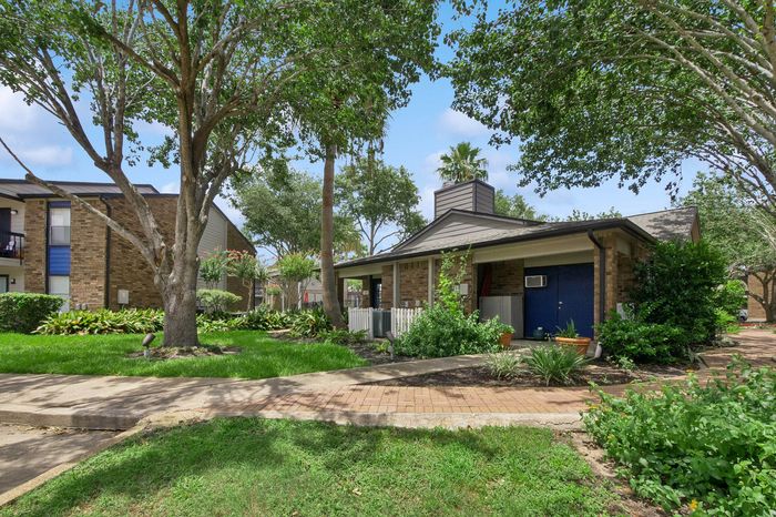 Charming apartment complex with brick structures nestled among lush green gardens and mature trees.