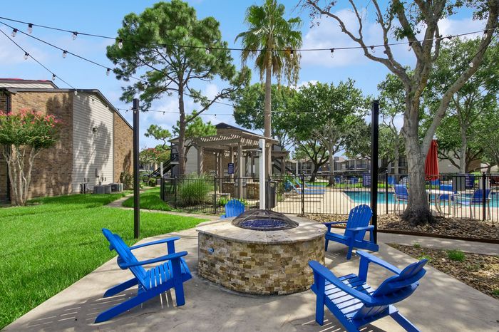 Charming outdoor community area featuring a cozy fire pit surrounded by vibrant blue chairs, lush green lawn, and a sparkling swimming pool under string lights.