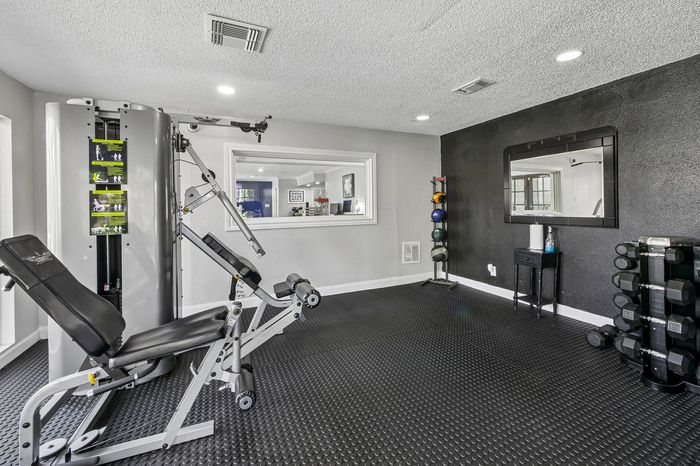 Modern home gym with sleek exercise equipment, including a multifunctional weight machine, kettlebell set, and dumbbells, on a black rubber floor.