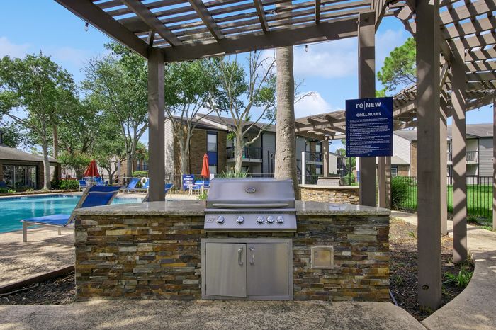 Charming outdoor grill area with modern amenities, nestled by a sparkling pool surrounded by lush greenery and comfortable lounge chairs.