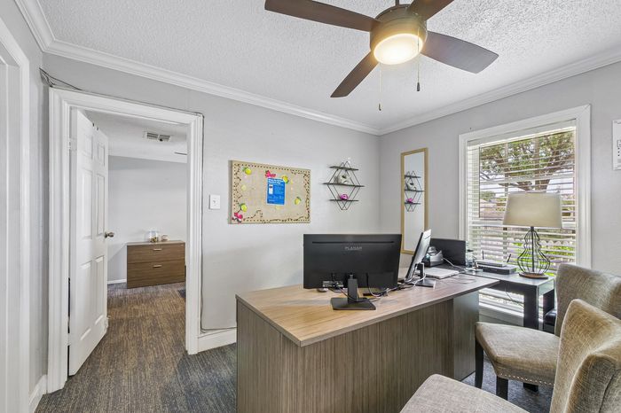 Contemporary home office with elegant decor, featuring a sleek wooden desk, comfortable seating, and natural light from a large window.