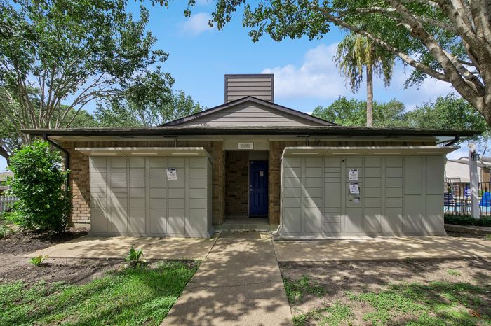 Charming building exterior with a blue door and shaded walkway, surrounded by lush greenery and beautiful trees.