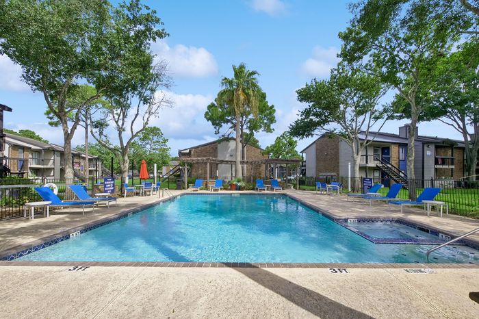 Inviting apartment complex pool area surrounded by lush greenery, lounge chairs, and a sunny, peaceful ambiance.