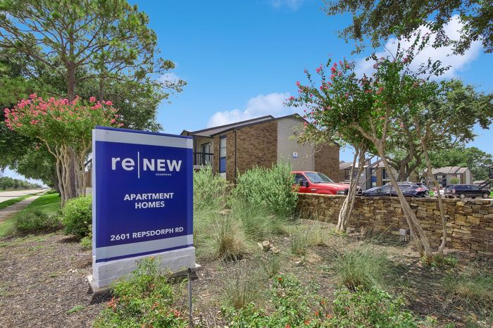 Welcoming entrance to ReNew Seabrook Apartment Homes with lush landscaping and vibrant blue skies, located at 2601 Repsdorph Rd.