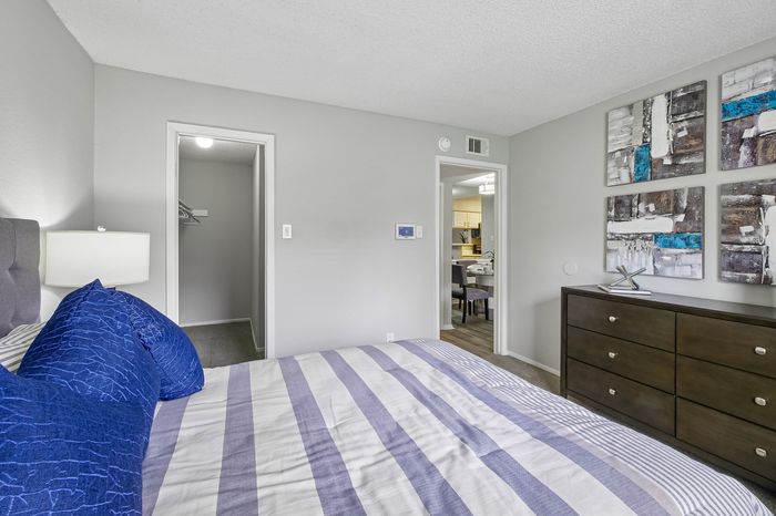 Inviting bedroom with modern decor, featuring a comfortable bed with striped bedding and vibrant blue pillows, overlooking a cozy kitchen dining area.
