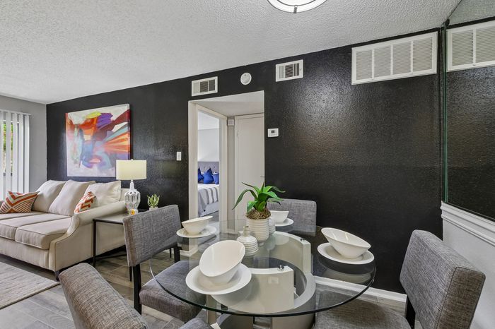 Sophisticated apartment dining area with a chic glass table set for four, cozy beige sofa, vibrant abstract art, and serene natural light enhancing the modern design.