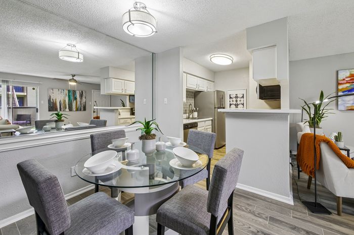 Chic dining area with a modern glass table set for four, adjacent to a sleek kitchen, complemented by elegant wall art and stylish furnishings.