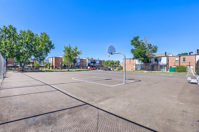 Inviting residential community with a spacious outdoor basketball court, surrounded by modern brick apartments and lush green trees under a clear blue sky.