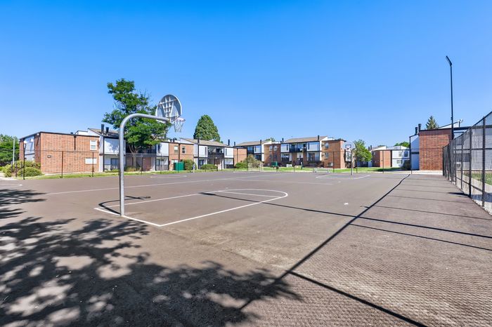 Inviting apartment complex with modern amenities, featuring a spacious outdoor basketball court under a clear blue sky.