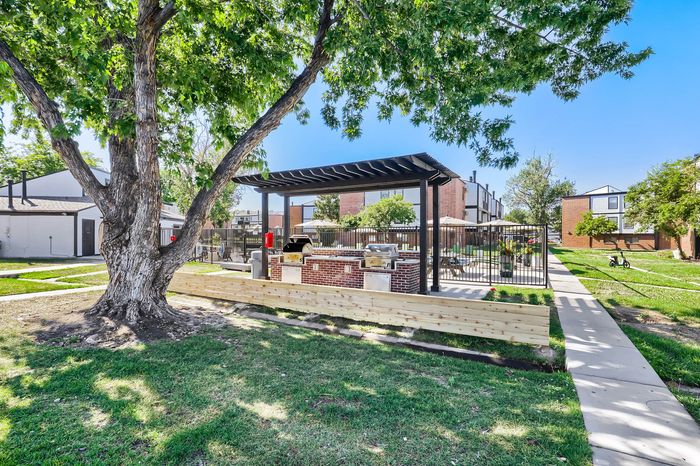 Charming outdoor patio area with BBQ grills under a stylish pergola, surrounded by lush greenery and modern apartments in the background.