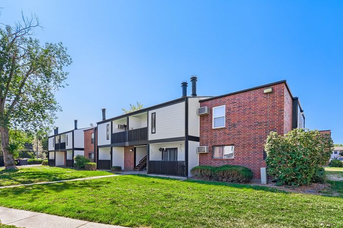 Charming modern apartment building with classic brick fa&ccedil;ade, lush green surroundings, and ample sunlight.