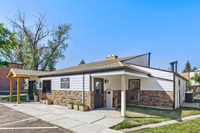 Welcoming leasing office with modern design, featuring stone accents and a cozy covered entrance under a clear sky.
