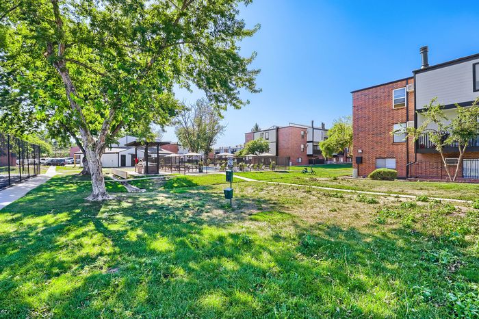 Inviting apartment complex with lush green spaces, modern buildings, and a peaceful outdoor area under a clear blue sky.