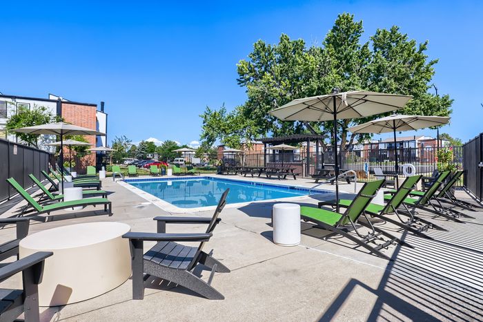 Inviting outdoor pool area with stylish sun loungers and umbrellas, set against a backdrop of lush greenery and modern apartments.