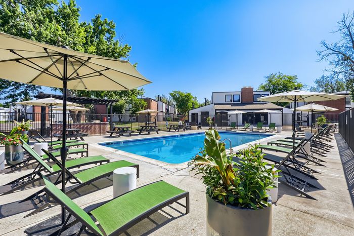 Inviting outdoor pool area with elegant lounge chairs, lush greenery, and relaxing umbrellas in a serene residential setting.