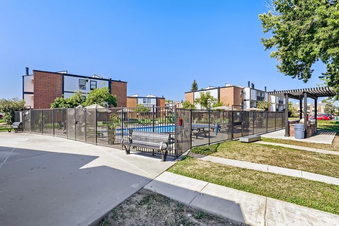 Modern apartment complex with a refreshing swimming pool, communal seating area, and lush green landscape, perfect for relaxation and leisure.