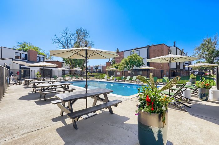 Inviting outdoor area with a sparkling pool, surrounded by lounge chairs and umbrellas, featuring lush greenery and modern picnic tables.