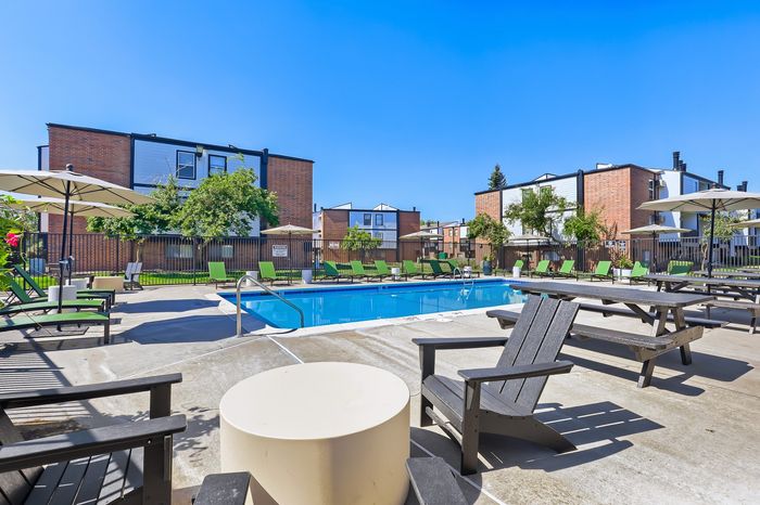Vibrant outdoor pool surrounded by lush greenery and modern seating, perfect for relaxation and leisure in a sunny apartment community.