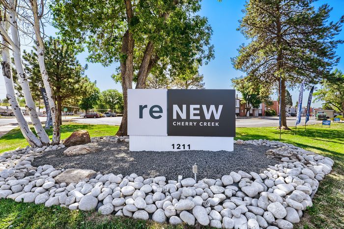 Inviting outdoor signage for ReNew Cherry Creek Apartments, surrounded by lush trees and decorative stones, creating a welcoming atmosphere.