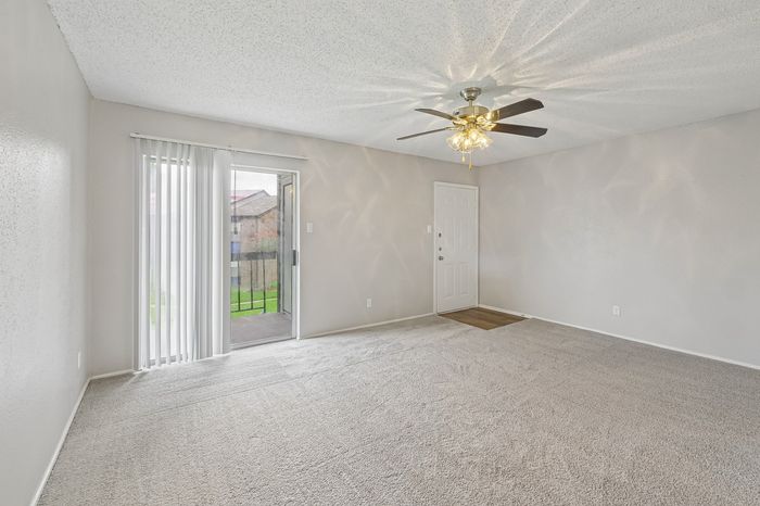 Bright and inviting living room with plush carpet, modern ceiling fan, and sliding glass door opening to a serene outdoor space.