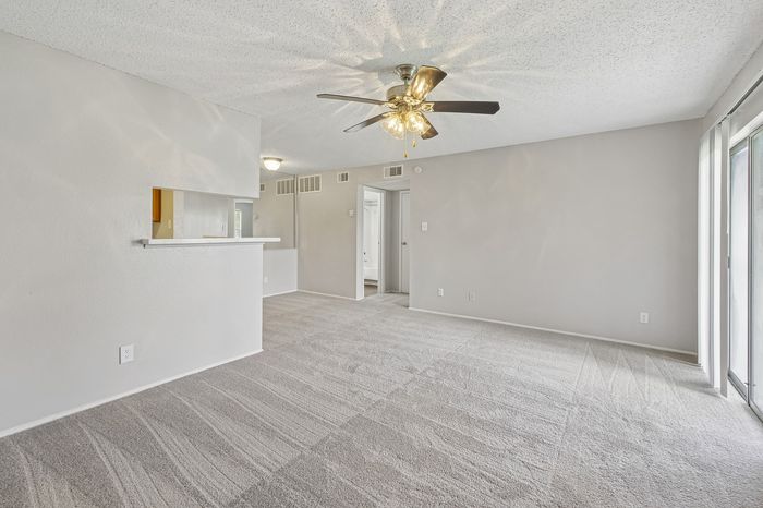 Bright, open-concept living space with plush carpet, ceiling fan, and abundant natural light from large windows.