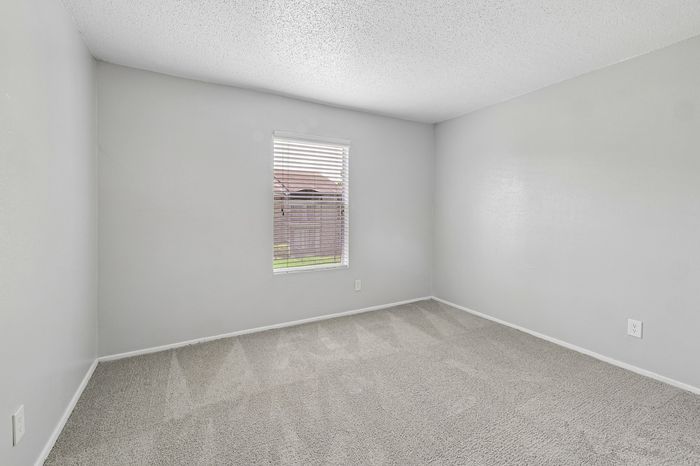 Bright and airy bedroom featuring plush carpet and a window with natural light, ideal for comfort and relaxation.