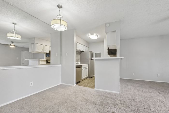 Bright modern living space with plush carpeting and contemporary lighting, adjacent to a sleek kitchen with stainless steel appliances.