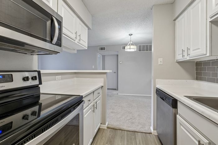 Modern kitchen featuring sleek stainless steel appliances, elegant white cabinetry, and a cozy open layout leading into a warm, inviting living space.