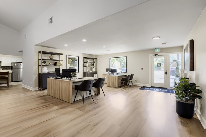 Modern office space with elegant wooden flooring, stylish desks, and comfortable seating, enhanced by natural light and decorative shelving.