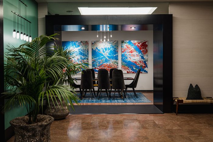 Modern dining area with elegant dark chairs, vibrant abstract artwork, and lush green plants for a stylish living experience.