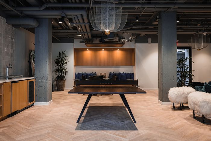 Modern communal area with stylish decor, featuring a ping-pong table, cozy seating with plush cushions, chic lighting, and sleek cabinetry.