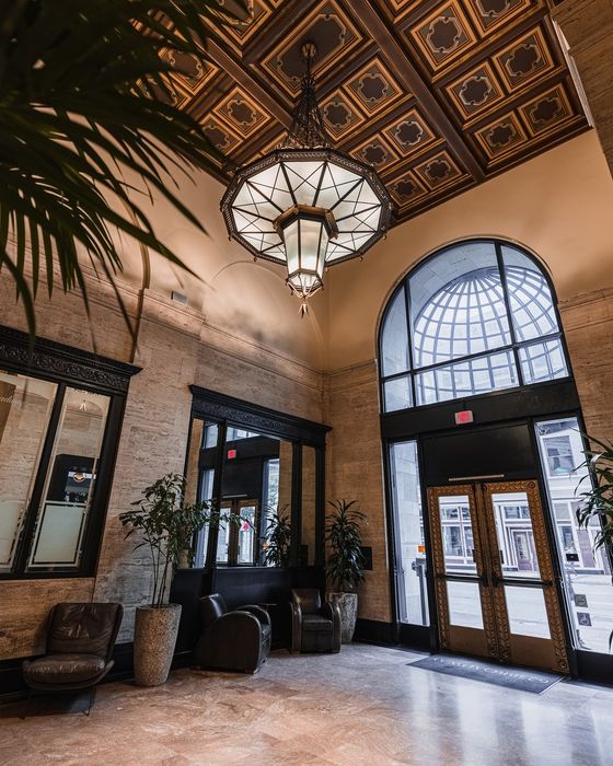 Opulent apartment lobby with a grand chandelier, intricate ceiling design, and inviting seating area surrounded by elegant potted plants.