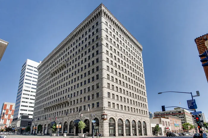 Impressive historic high-rise with elegant architecture and street-level shops, basking under clear blue skies in a lively urban setting.